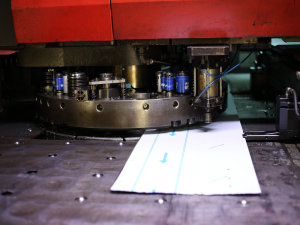 מכונת ניקוב AMADA - בעבודה על פח מתכת מכוסה PVC, כחלק מיצור סדרתי. ברצפת היצור של א.ד.ה.פ תעשיות.